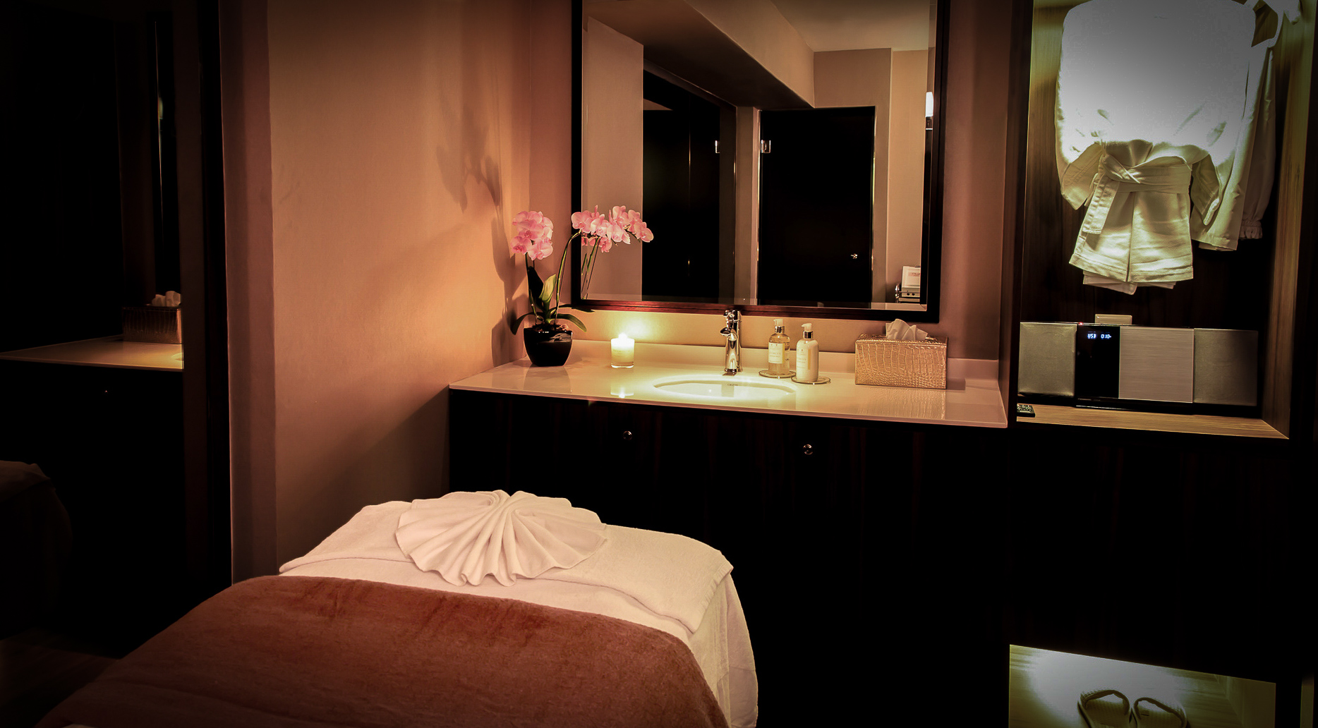 A candlelit Frances treatment room with orchids and folded towels